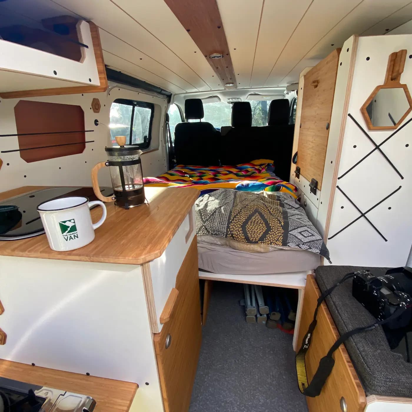 Intérieur d'un van aménagé électrique, plan de travail en bois, cafetière à piston et couchage